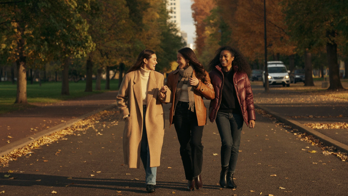 Drei Frauen in Herbstmode lachen gemeinsam in einer herbstlichen Allee